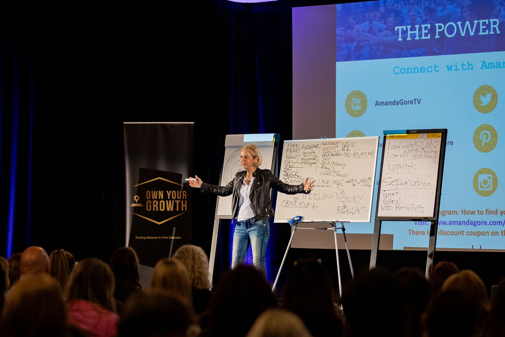 Amanda Gore, leadership keynote speaker, teaching at three flip charts on the Own Your Growth conference stage