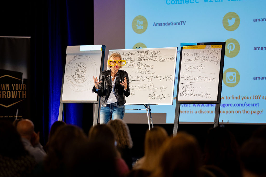 Amanda Gore, leadership keynote speaker, at the flip charts as the audience makes glasses with their hands