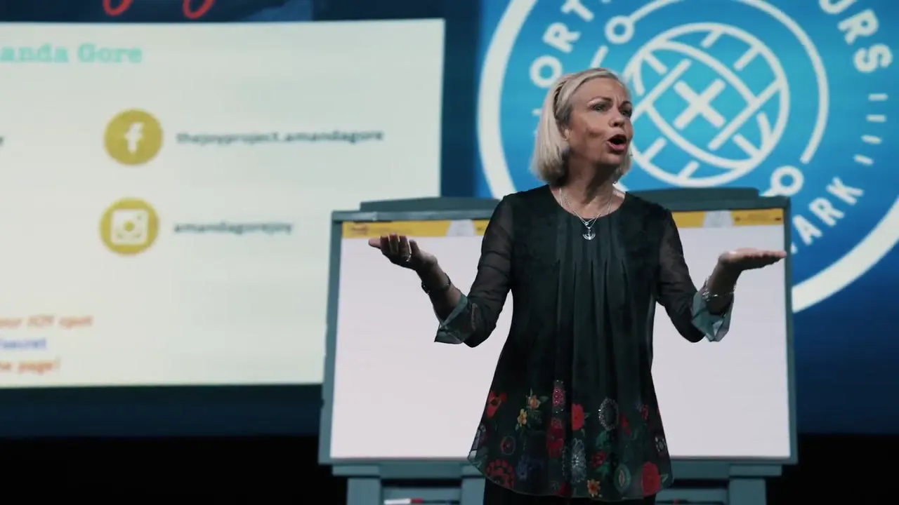 Amanda Gore, leadership keynote speaker, on stage with her arms out, asking the audience a question