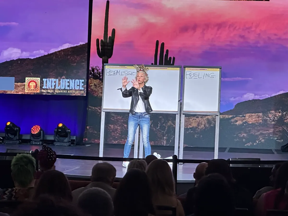 Amanda Gore, leadership keynote speaker, on the INFLUENCE stage in front of a desert sunset screen