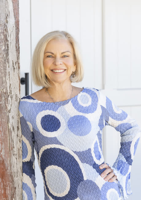 Amanda Gore, leadership speaker, smiling, leaning on a wooden post