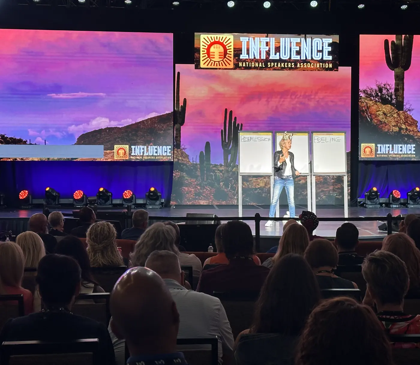 Amanda Gore, leadership keynote speaker, delivering a keynote on the INFLUENCE main stage at the flip charts, with the audience in front of her