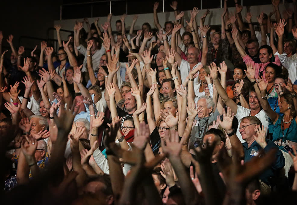 Conference audience with hands raised during an Amanda Gore keynote