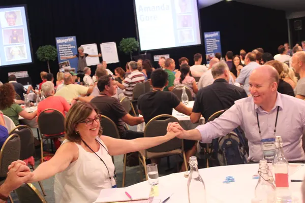 Audience members joining hands across a table at an Amanda Gore keynote