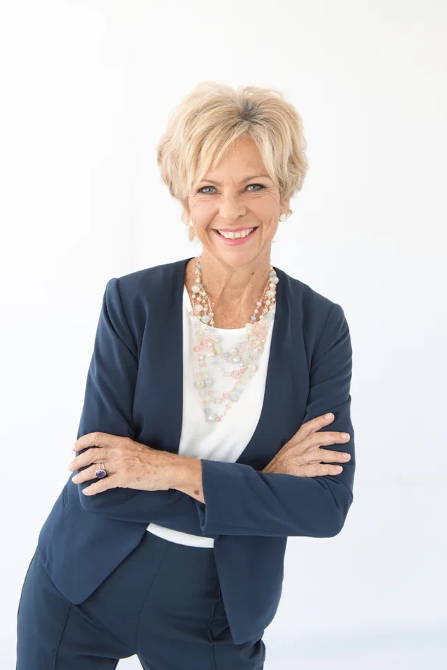 Amanda Gore, leadership keynote speaker, smiling with her arms folded, in a navy jacket and a pastel beaded necklace