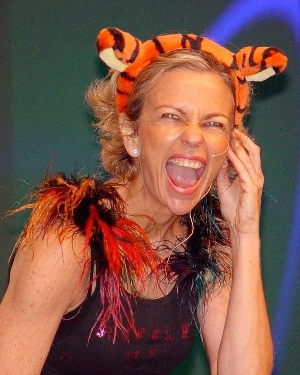 Amanda Gore, leadership speaker, laughing out loud on stage in tiger ears and a feather boa