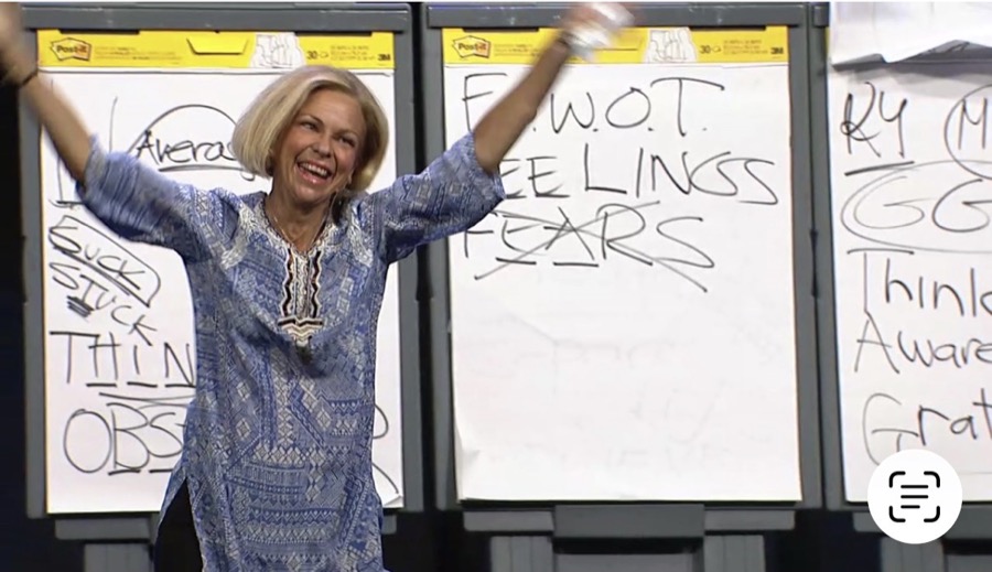 Amanda Gore, leadership keynote speaker, close up, arms raised and laughing beside her flip charts