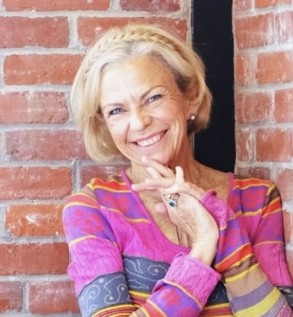 Amanda Gore, leadership keynote speaker, smiling against a brick wall in a bright striped top