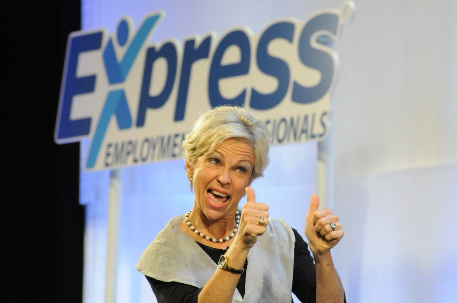 Amanda Gore, leadership keynote speaker, on stage at Express Employment Professionals, smiling and giving two thumbs up