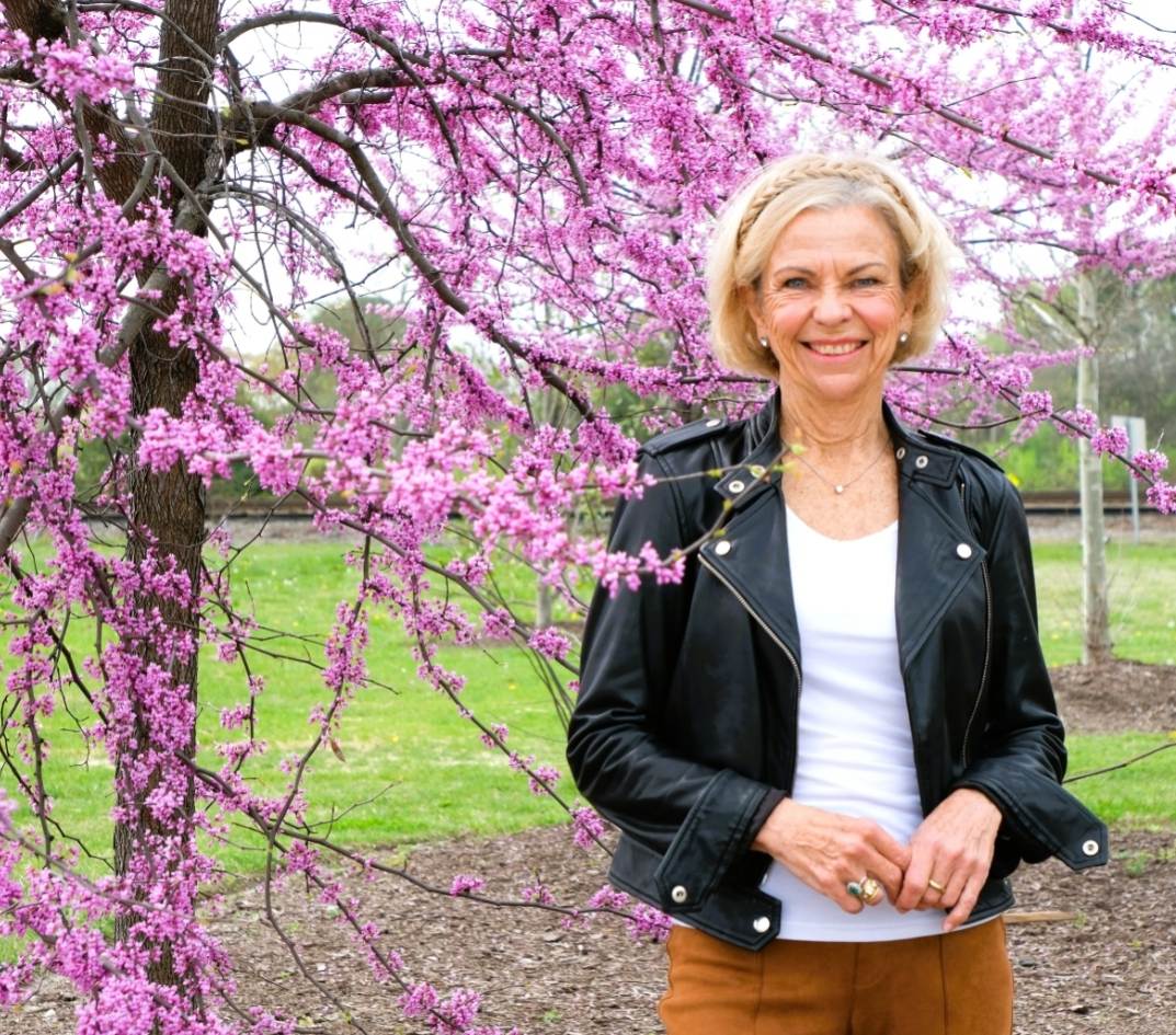 Amanda Gore, leadership keynote speaker, smiling in a black leather jacket beside a tree in pink blossom