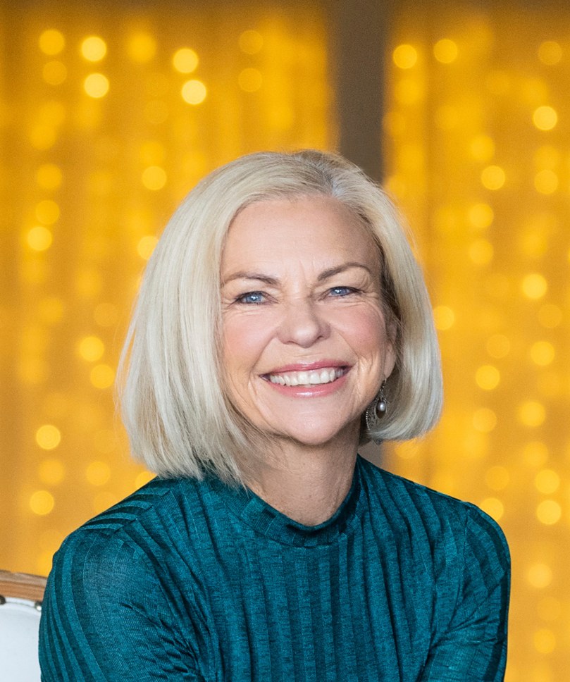 Amanda Gore smiling in a teal top in front of golden lights