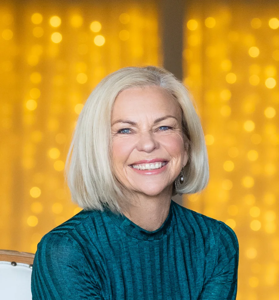 Amanda Gore, leadership keynote speaker, smiling in a teal top in front of golden lights