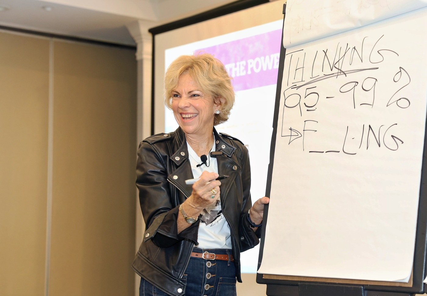 Amanda Gore, leadership speaker, laughing beside a flip chart in a leather jacket
