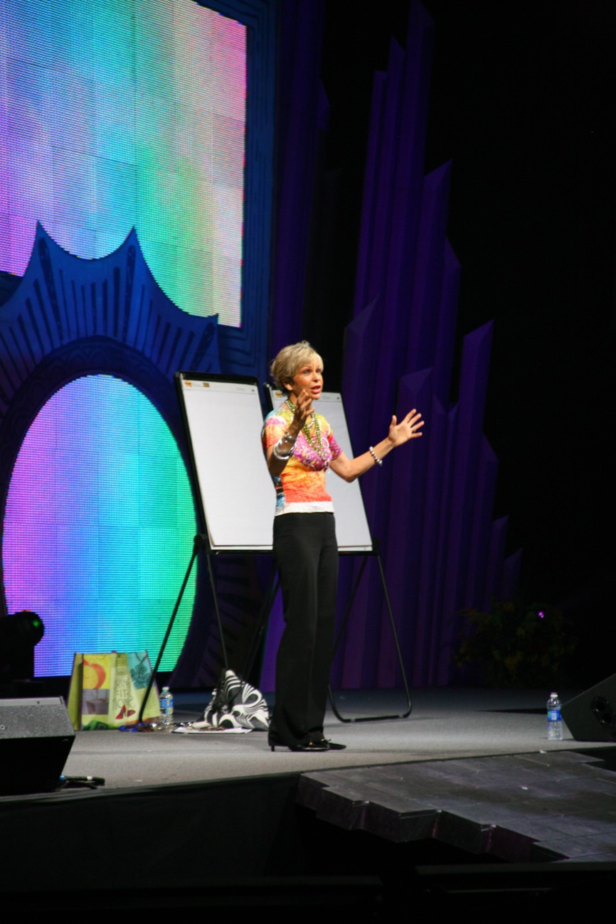 Amanda Gore, leadership keynote speaker, on a colorful stage beside her flip chart, speaking to the audience