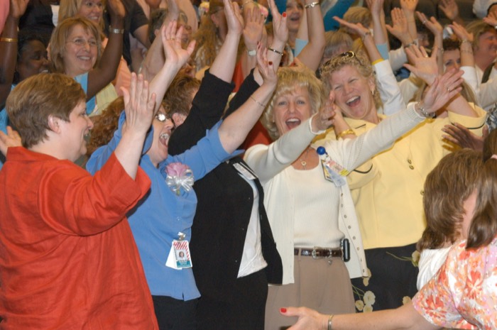 An audience on its feet with arms raised, cheering at an Amanda Gore keynote
