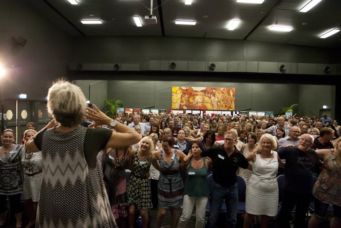 Amanda Gore from behind, facing a standing audience at a keynote