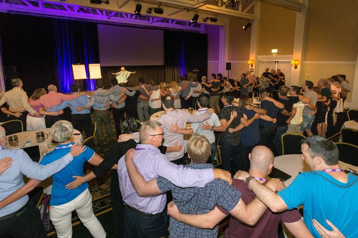 An audience arm in arm, dancing together at an Amanda Gore keynote