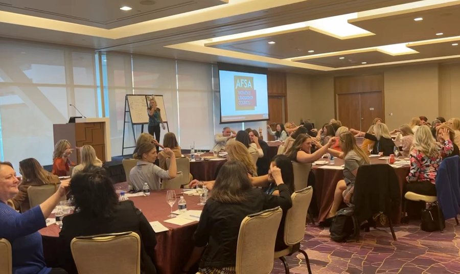 Amanda Gore at her flip charts with a room of leaders at round tables, at the AFSA Women’s Leadership Council