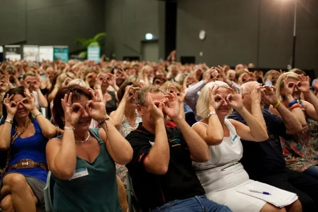 An audience at an Amanda Gore keynote making glasses with their hands